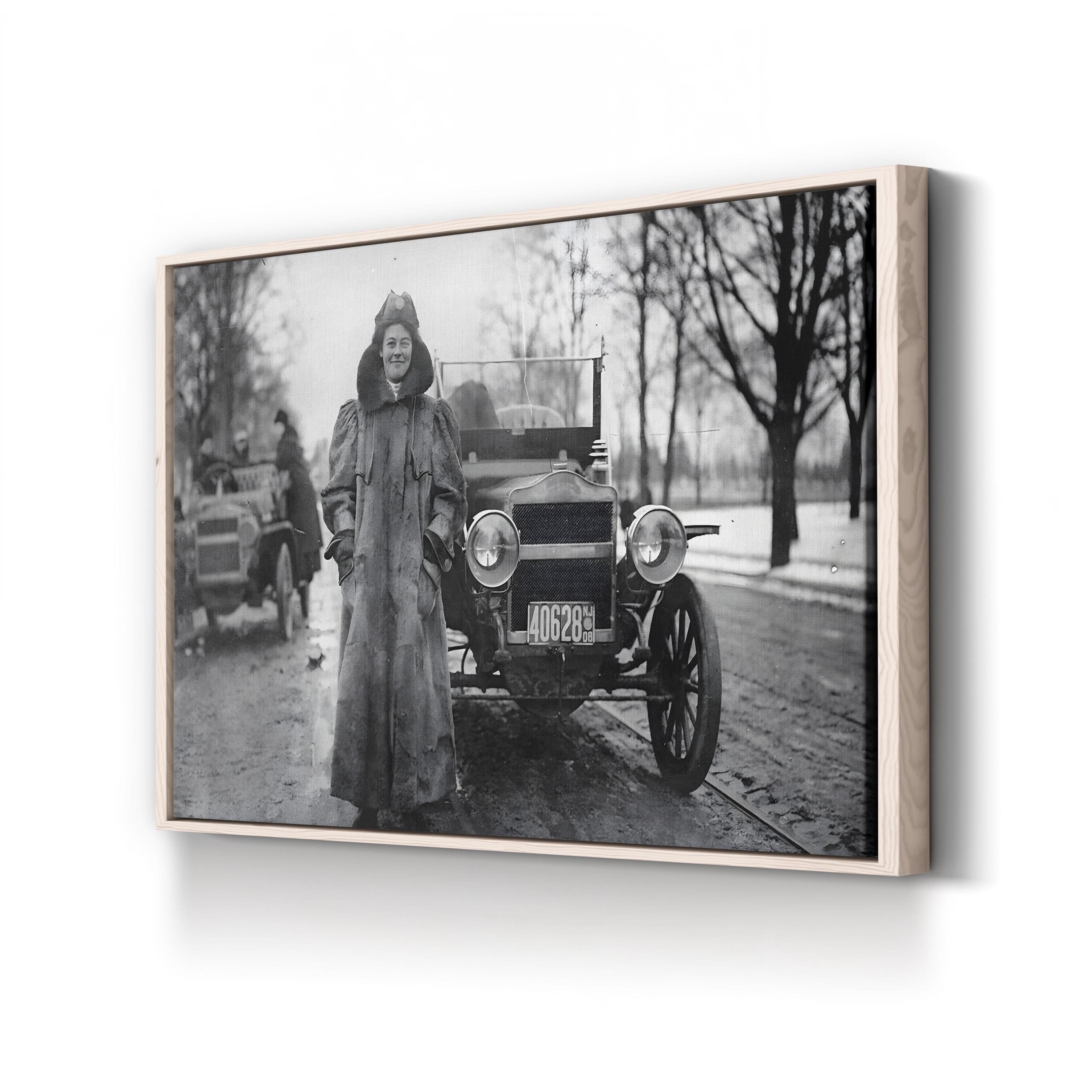 Framed black and white photograph of a woman standing next to an old car on a snowy street.