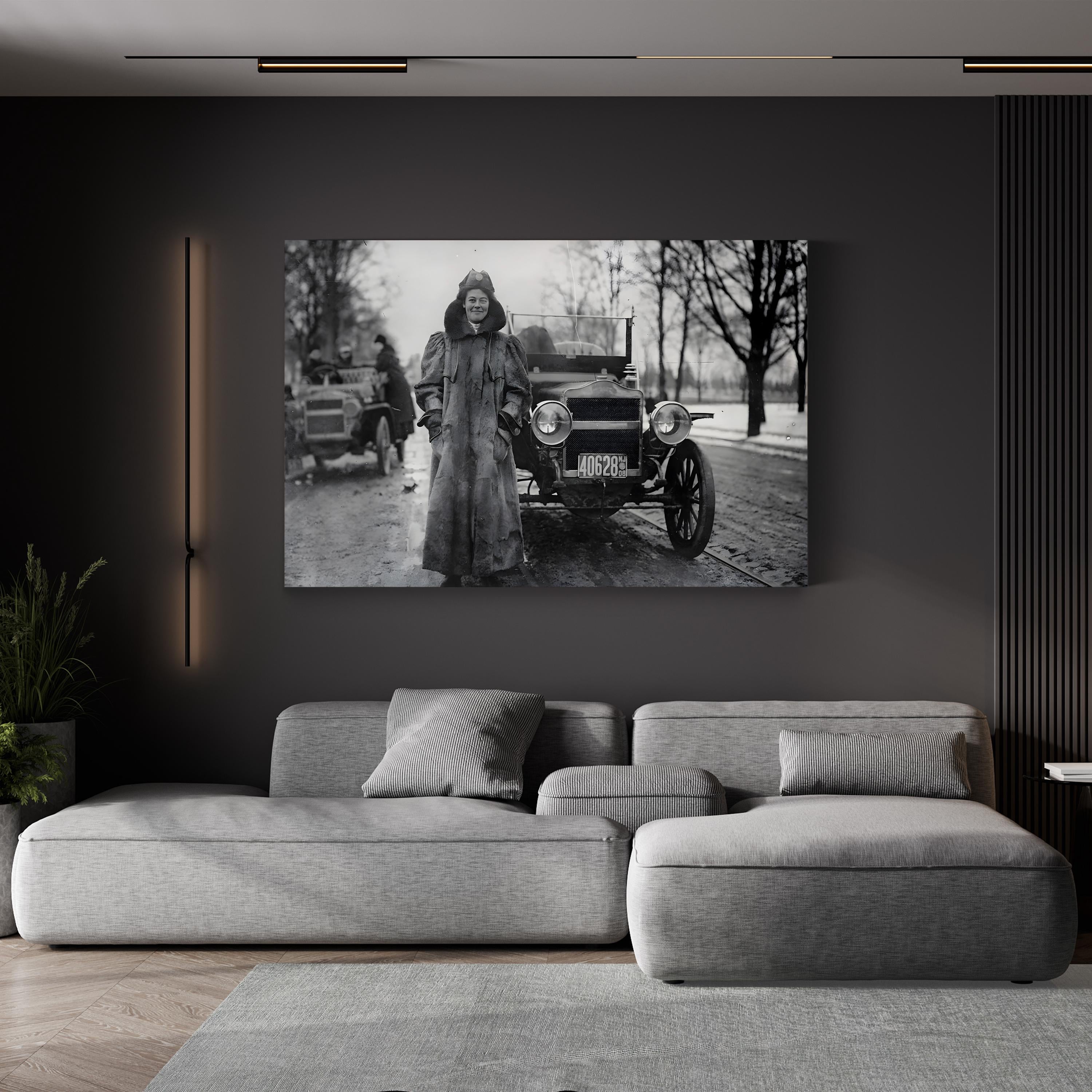 Gray sectional sofa in a living room with a black and white photograph of a woman in a coat standing next to an old car on the wall.